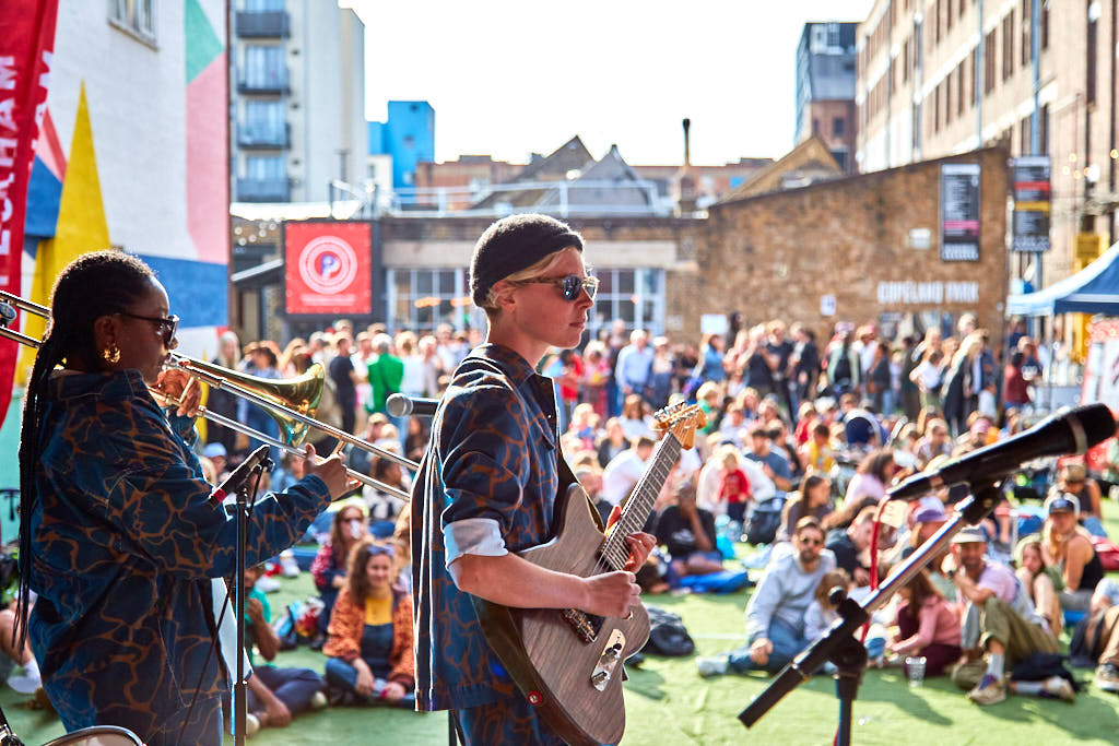 Band playing on an outdoor stage to a crowd sitting on the grass