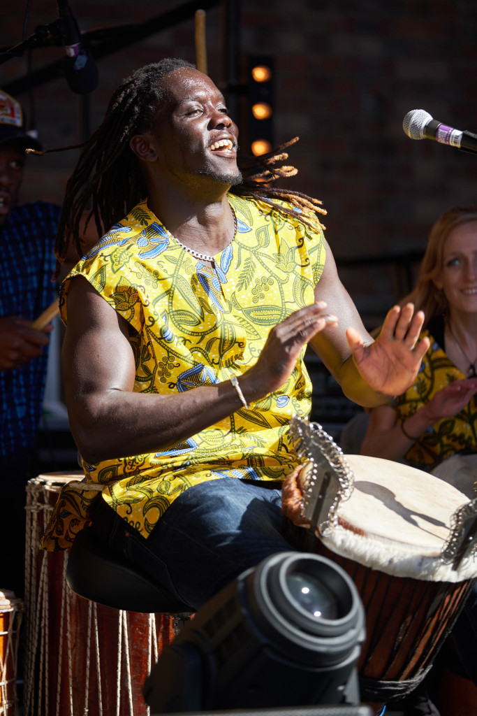 Smiling drummer in a yellow shirt playing a djembe
