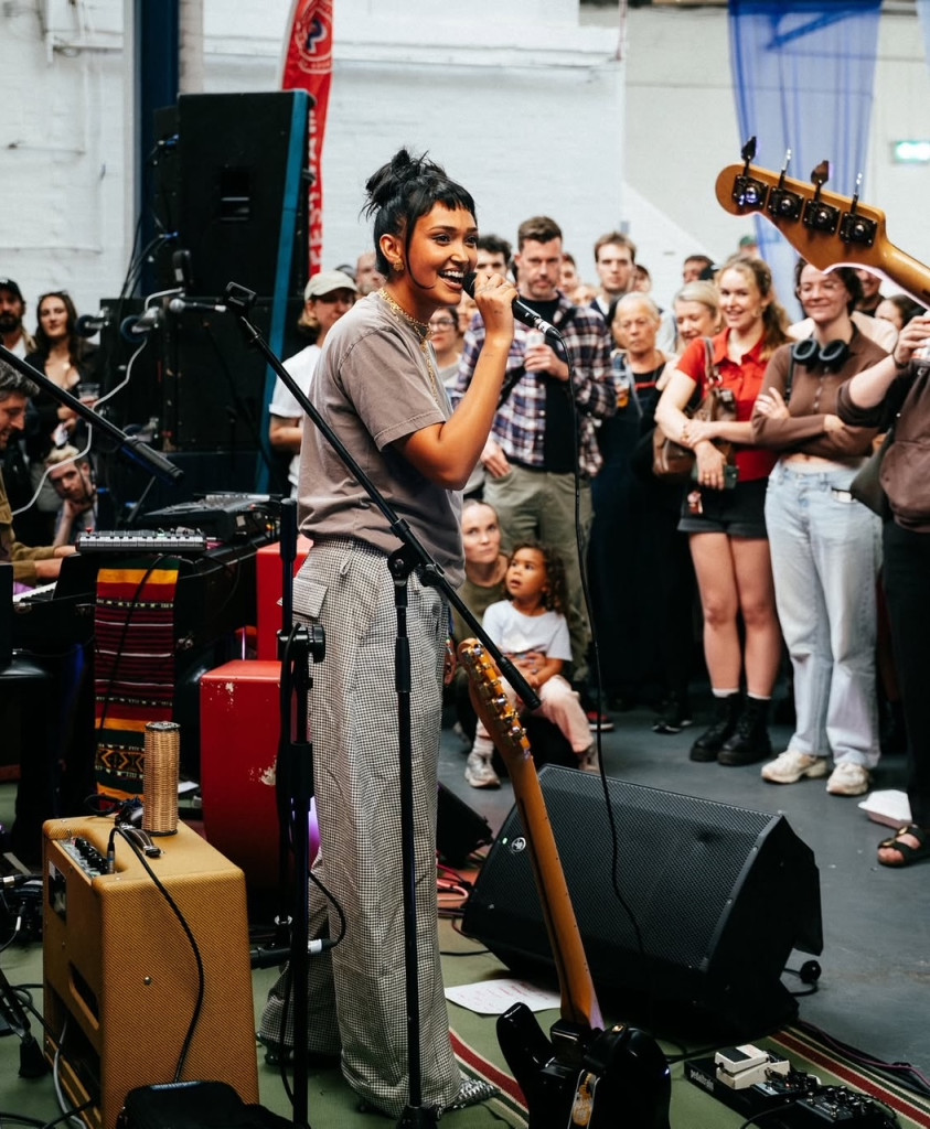 Performer singing into a microphone in front of a crowd at an indoor gig
