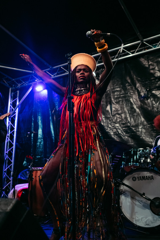 Singer in a tasselled costume raising an arm on a lit stage